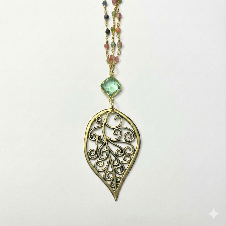 Gold leaf-shaped pendant with a green gemstone on a white background
