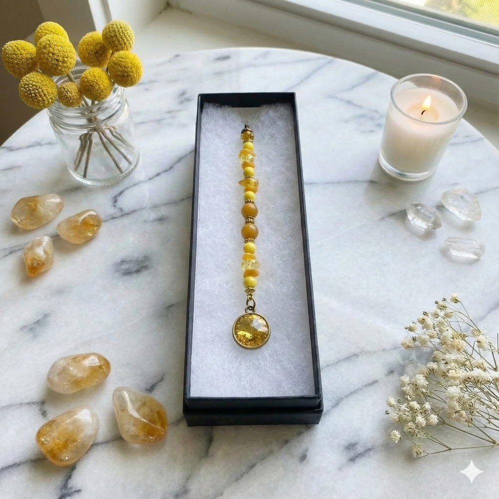 Amber beaded necklace in a box on a marble surface with yellow flowers and candles.